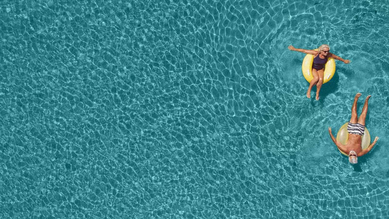 Senior couple floating in pool on inflatables in Greece.