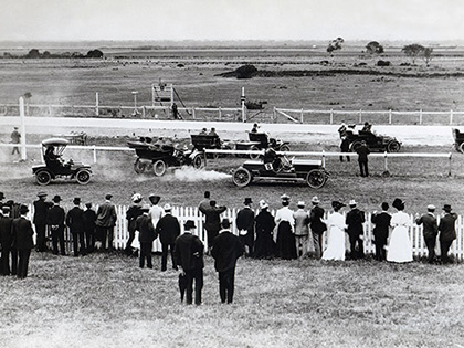 Cars racing on the Aspendale Park Racecourse track as a crowd of people watch from the sidelines in 1904.