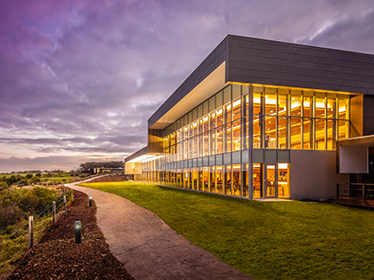 Path surrounded by greenery leading to the main RACV Inverloch Resort building, lit up at dusk.