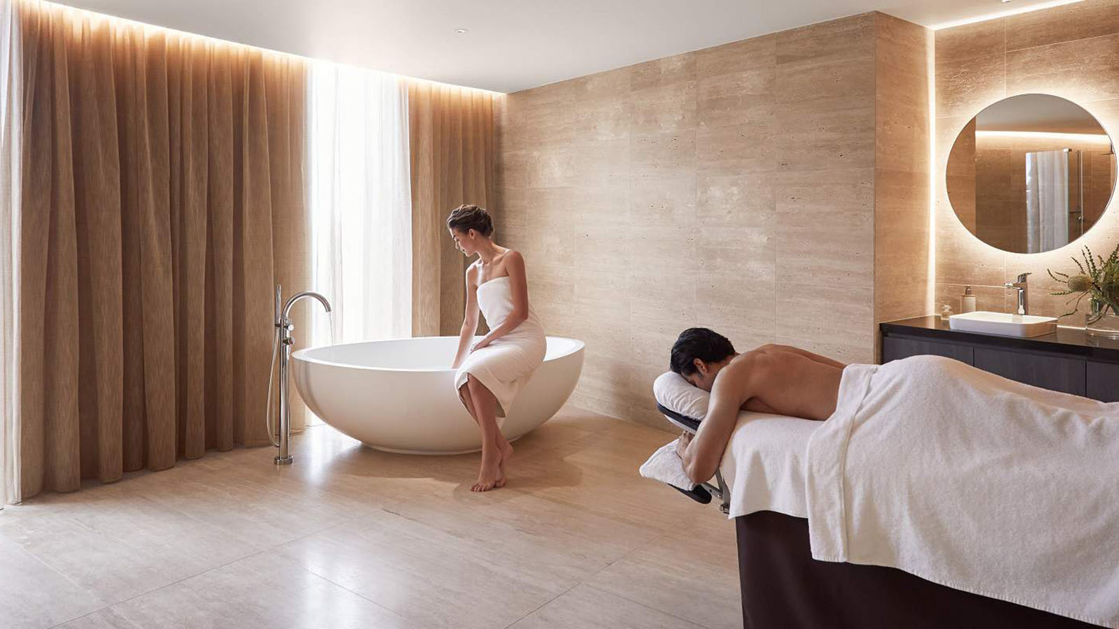 Couple enjoying treatment at RACV One Spa, woman filling a bath while man lies on a massage table.