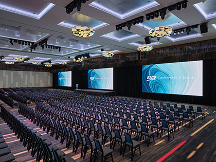 Royal Benowa Ballroom at RACV Royal Pines Resort, set up theatre style with three screens behind a stage.