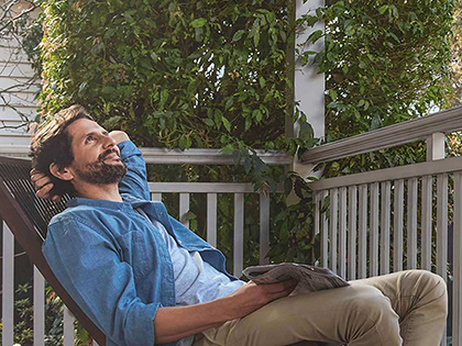 man relaxing on balcony with newspaper in hand