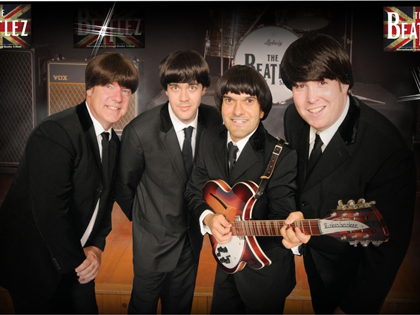 Four men dressed in suits impersonating the beatles. 
