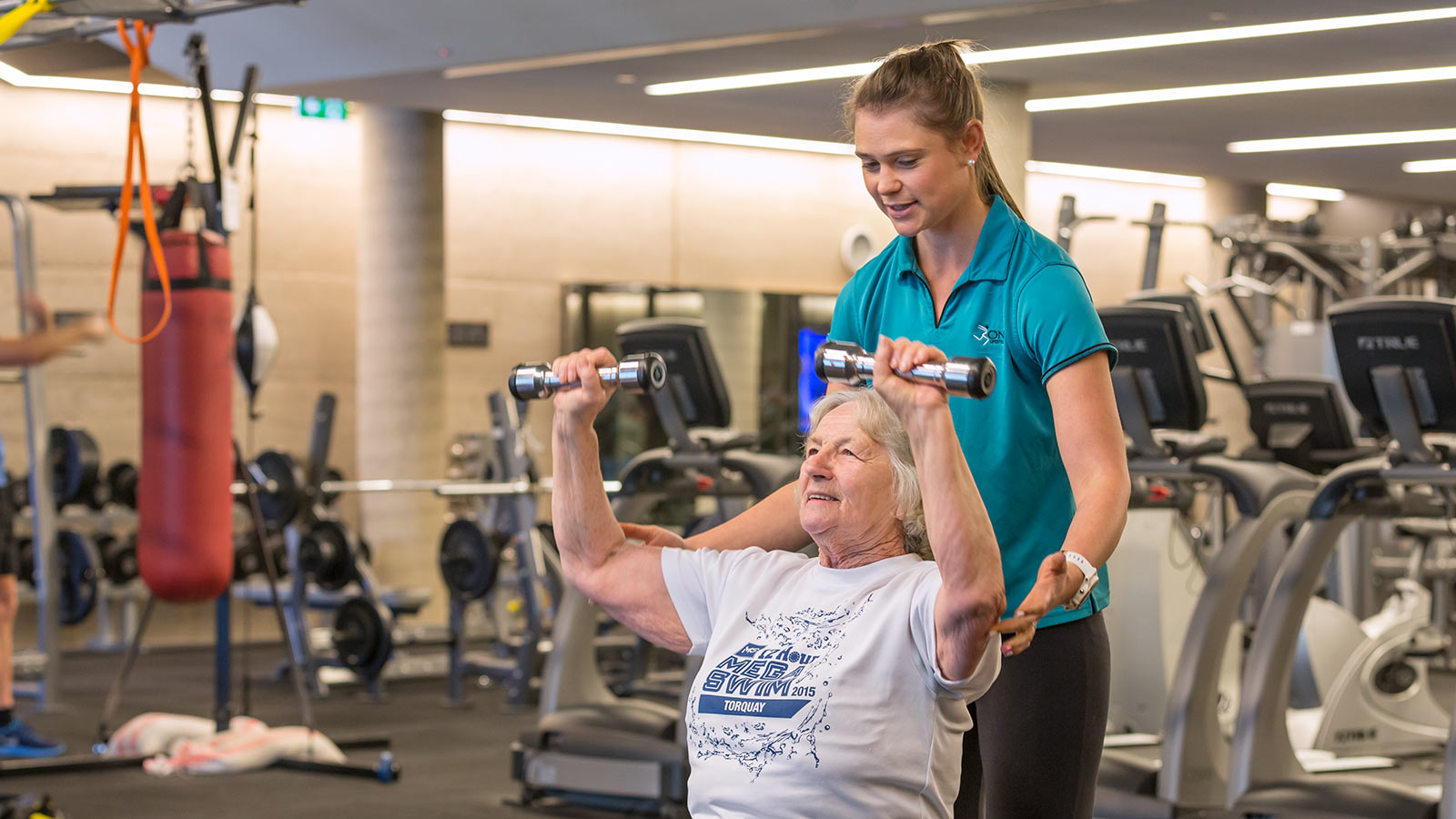 Personal trainer guiding senior through exercise with dumbbells at RACV Torquay Resort's One Lifestyle fitness centre.