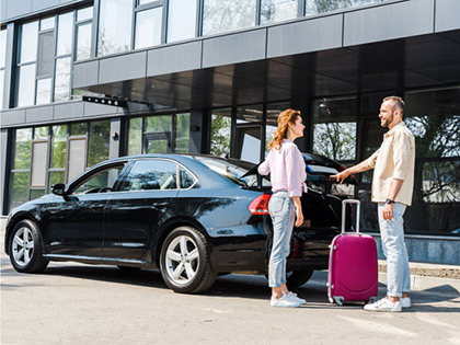 Two people taking their luggage out of a parked black car.