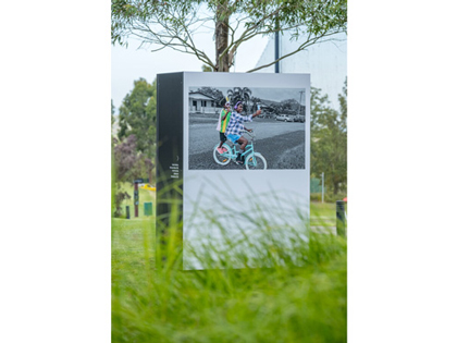 Large block installation in a grassy park, displaying a photograph of a person riding a bicycle.