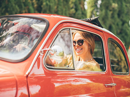 Woman wearing sunglasses sitting in a red, vintage car.