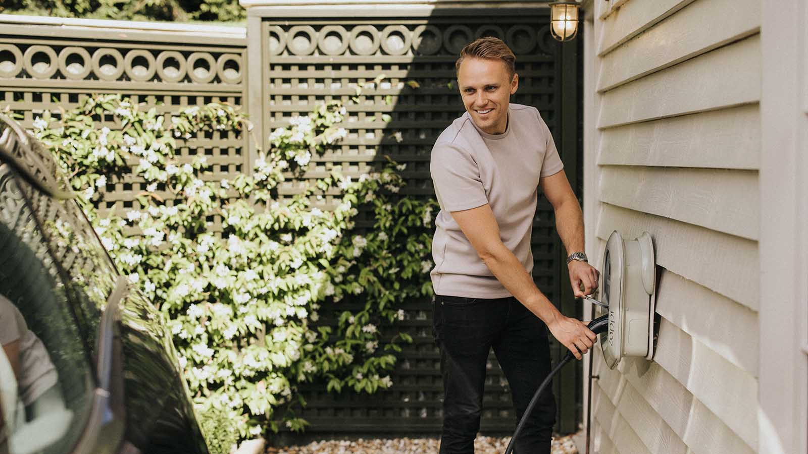 Man in back yard charging an electric vehicle with the Zappi home charger.